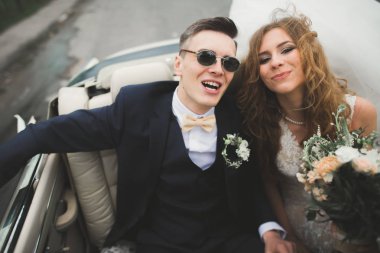 Şık bir düğün çifti, gelin, damat retro arabada öpüşüyor ve sarılıyor.