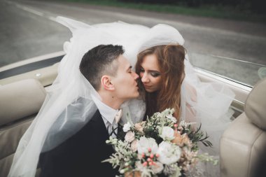 Şık bir düğün çifti, gelin, damat retro arabada öpüşüyor ve sarılıyor.