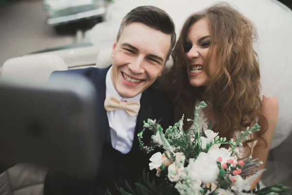 Happy bride and groom making selfie at their wedding in retro car — Stock Photo, Image