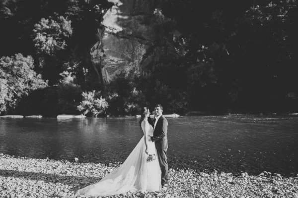 Элегантная стильная счастливая блондинка-невеста и великолепный жених на фоне красивой реки в горах — стоковое фото