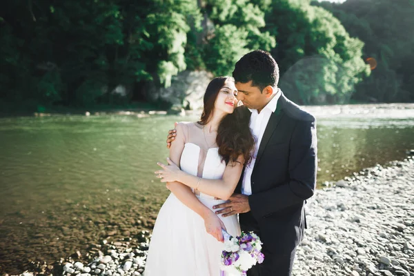 Düğün çifti, damat ve gelin kucaklaşıyor, nehir kenarında. — Stok fotoğraf