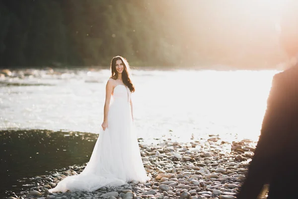 Elegante novia rubia feliz y elegante novio en el fondo de un hermoso río en las montañas —  Fotos de Stock