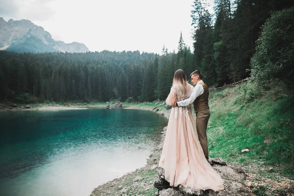 Doğadaki düğün çifti, dağlardaki güzel bir gölün yanında birbirlerine sarılıyorlar beyaz elbiseli güzel model kız. Takım elbiseli adam — Stok fotoğraf