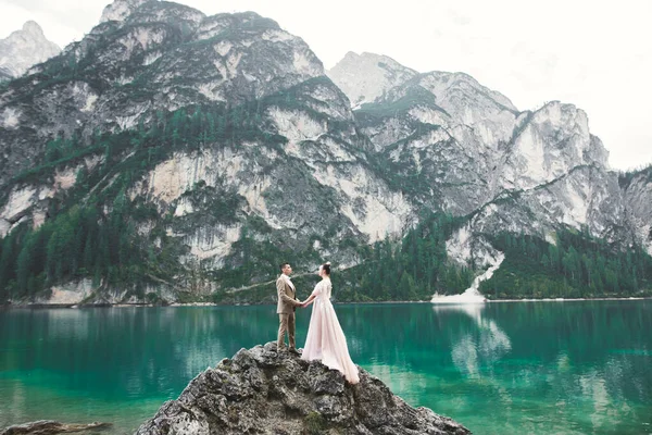 Casal jovem perto do lago Karersee, Itália. De mãos dadas na pedra no lago — Fotografia de Stock