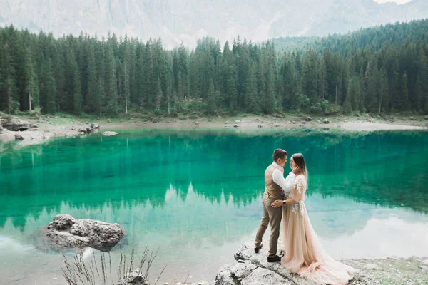 Γάμος ζευγάρι στη φύση αγκαλιάζει ο ένας τον άλλον κοντά σε μια όμορφη λίμνη στα βουνά.. Όμορφο κορίτσι μοντέλο σε λευκό φόρεμα. Άνδρας με κοστούμι — Φωτογραφία Αρχείου