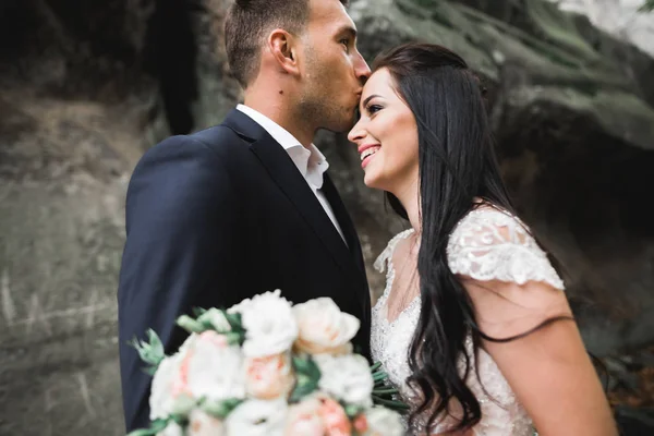 Mooi jong bruidspaar poseren met boeket bloemen in handen — Stockfoto