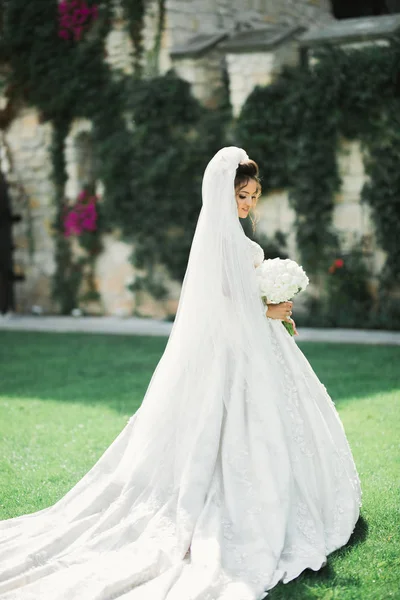 Hermosa novia en elegante vestido blanco sosteniendo ramo posando en el parque —  Fotos de Stock