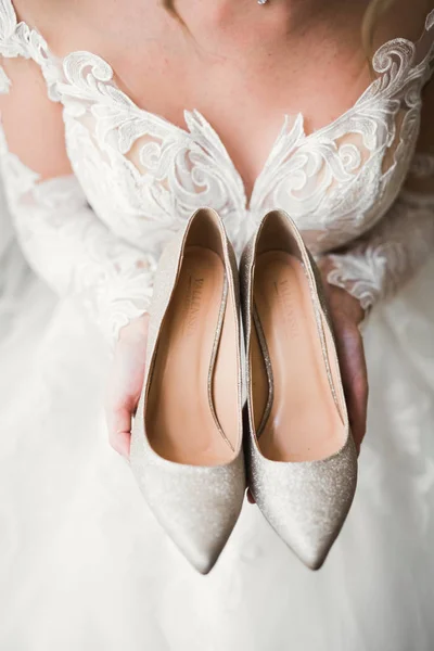 Piękne luksusowe panny młodej w eleganckiej białej sukience posiada buty ślubne w rękach — Zdjęcie stockowe