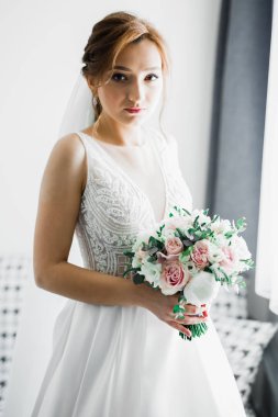 Çekici gelinin portresi, uzun saçlı, büyük buketli poz veren.