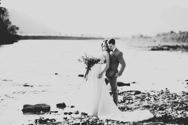 Romántico, cuento de hadas, feliz pareja recién casada abrazándose y besándose con árboles y río en el fondo —  Fotos de Stock
