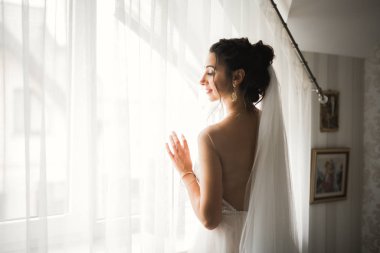 Cüppeli muhteşem gelin bir odada düğün töreni için poz veriyor ve hazırlanıyor.