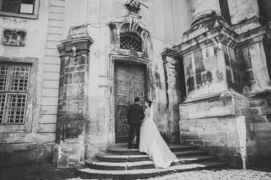 Düğün fotoğrafı çekimi. Gelin ve damat şehirde yürüyorlar. Birbirlerine sarılıp bakan evli bir çift. Tutma buketi