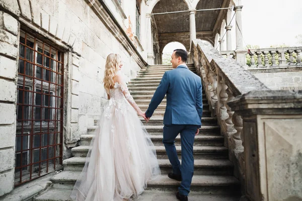 Mooi bruidspaar klimmend op een prachtige trap hand in hand en kijkt naar elkaar — Stockfoto
