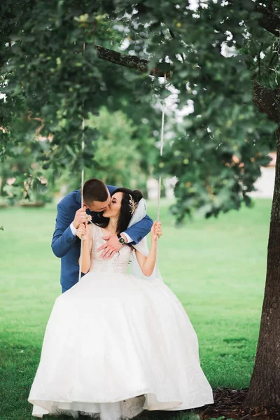 Romantický, pohádkový, šťastný novomanželský pár objímající a líbající se v parku, stromy v pozadí — Stock fotografie