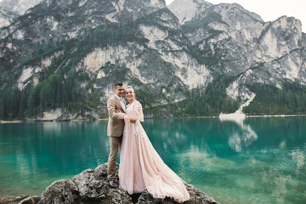 Hochzeitspaar in der Natur umarmt einander in der Nähe eines schönen Sees in den Bergen.. Schöne Modell Mädchen in weißem Kleid. Mann im Anzug — Stockfoto