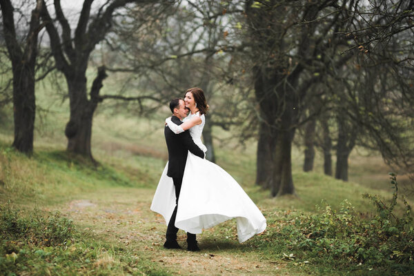 Romantic, fairytale, happy newlywed couple hugging and kissing in a park, trees in background.