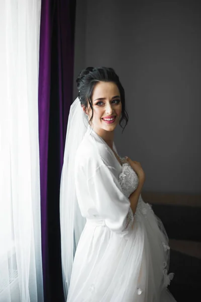 Linda noiva em roupão posando e se preparando para o rosto cerimônia de casamento em uma sala — Fotografia de Stock