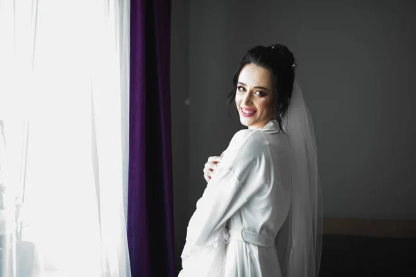 Linda noiva em roupão posando e se preparando para o rosto cerimônia de casamento em uma sala — Fotografia de Stock