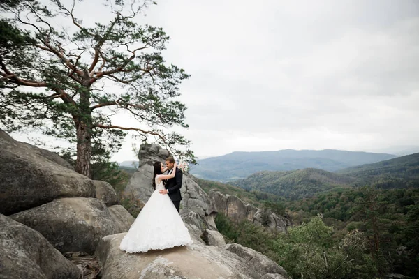 Όμορφη πανέμορφη νύφη που ποζάρει στον γαμπρό και διασκεδάζει κοντά στα βουνά με καταπληκτική θέα, χώρος για κείμενο, ζευγάρι γάμου — Φωτογραφία Αρχείου