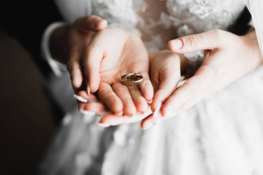 Zarif beyaz elbiseler içinde güzel bir gelin ve damat ellerinde alyansları tutuyor.