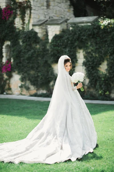 Hermosa novia en elegante vestido blanco sosteniendo ramo posando en el parque —  Fotos de Stock