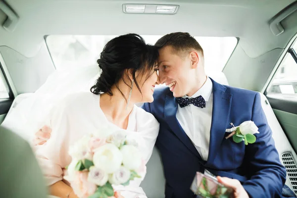 Bellissimi sposi che si abbracciano e si baciano il giorno del loro matrimonio in auto — Foto Stock