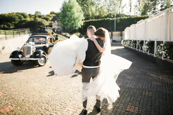 Novia de boda y novio, pareja elegante alojándose cerca de coche de boda retro — Foto de Stock