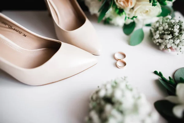 Par de zapatos de novia elegantes y elegantes con anillos de boda y un ramo de rosas y otras flores — Foto de Stock