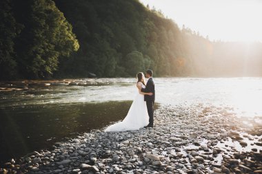 Düğün çifti, damat ve gelin kucaklaşıyor, nehir kenarında.