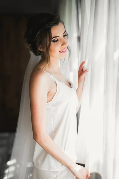 Preciosa novia en bata posando y preparándose para la ceremonia de boda cara en una habitación —  Fotos de Stock