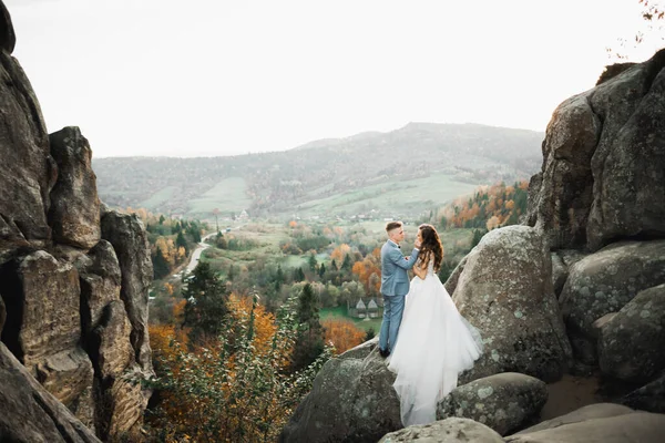 Linda noiva linda posando para noivo e se divertindo perto de montanhas com vista incrível, espaço para texto, casal de casamento — Fotografia de Stock