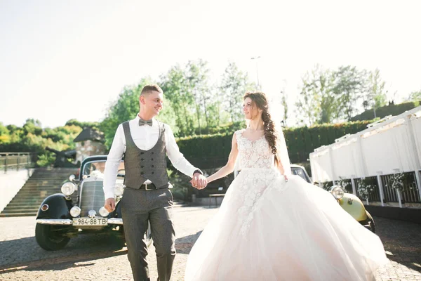 Düğün çifti, güzel gelin ve zarif damat el ele tutuşup birbirlerine retro düğün arabasının yanında bakıyorlar. — Stok fotoğraf
