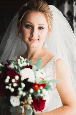 Zarif beyaz elbiseli güzel gelin elinde bir buket çiçek tutuyor.
