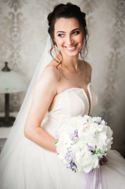 Cüppeli muhteşem gelin bir odada düğün töreni için poz veriyor ve hazırlanıyor.