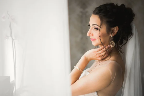 Preciosa novia en bata posando y preparándose para la ceremonia de boda cara en una habitación — Foto de Stock