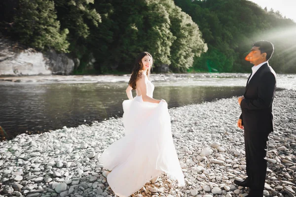 Elegante noiva loira feliz e lindo noivo no fundo de um belo rio nas montanhas — Fotografia de Stock