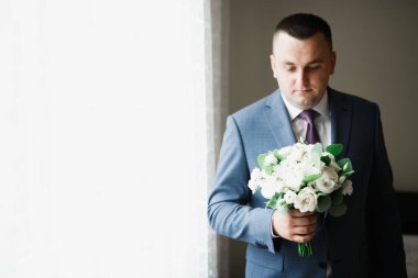 Güzel adam, damat elinde çiçeklerle büyük ve güzel bir düğün buketi tutuyor