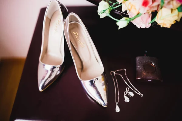 Brides wedding shoes and costume jewellery with a bouquet with roses and other flowers.