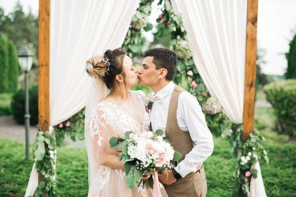 Piękna panna młoda i pan młody obejmujący i całujący się w dniu ślubu na świeżym powietrzu — Zdjęcie stockowe