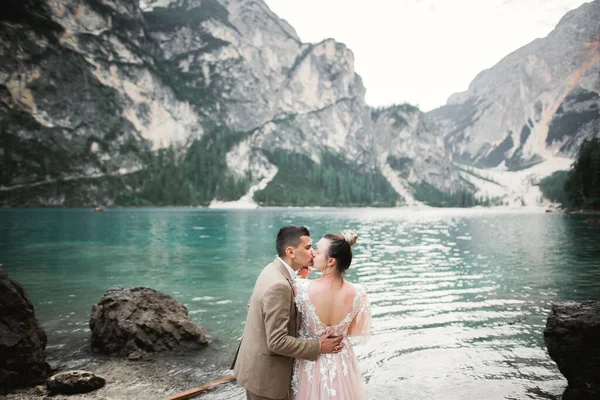 Casamento casal na natureza está abraçando uns aos outros perto de um belo lago nas montanhas.. Menina modelo bonita em vestido branco. Homem de fato — Fotografia de Stock