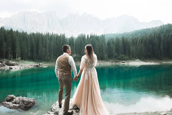 Pareja joven cerca del lago Karersee, Italia. Tomando de la mano en la piedra en el lago —  Fotos de Stock