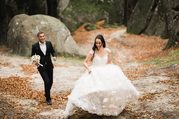 Couple élégant de jeunes mariés heureux. Mariée fuyant le marié dans le parc le jour de leur mariage avec bouquet — Photo