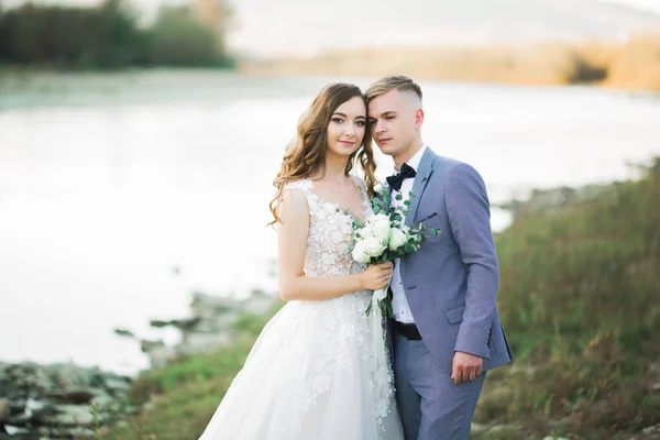 Elegante stilvolle glückliche blonde Braut und wunderschöner Bräutigam vor dem Hintergrund eines schönen Flusses in den Bergen — Stockfoto