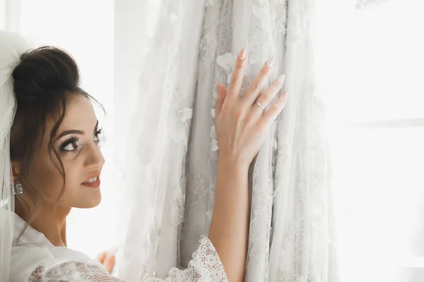 Preciosa novia en bata posando y preparándose para la ceremonia de boda cara en una habitación — Foto de Stock