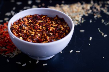 Koyu arkaplanda beyaz bardakta kırmızı biber, dağınık pirinç.