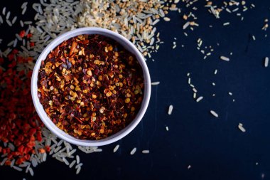 Koyu arkaplanda beyaz bardakta kırmızı biber, dağınık pirinç.