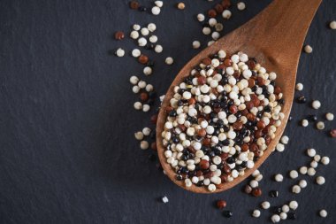Karışık ham quinoa (Chenopodium quinoa). Kırmızı, tahta kaşık siyah arka plan üzerine siyah ve beyaz tohumları. Kopya alanı ile Üstten Görünüm