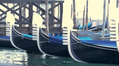 Bu stok videoda İtalya, Venedik 'teki Grand Canal' da park etmiş gondolların yavaş çekim görüntüleri var. Gondollar mavi örtülerle korunuyor ve tahta direklere bağlanıyor..