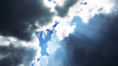 This stock video features a dense cloud formation in the morning. Darkness surrounds the cloud, but the sunlight can still be seen up above, hiding behind the clouds. 