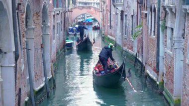 Venedik 'in Kanal stok görüntülerinde Venedik kanallarında yüzerken turistler bir gondola biniyor. Venedik 'in kanal kenarındaki eski evleri ve kemerli köprüler klipte görülebilir..